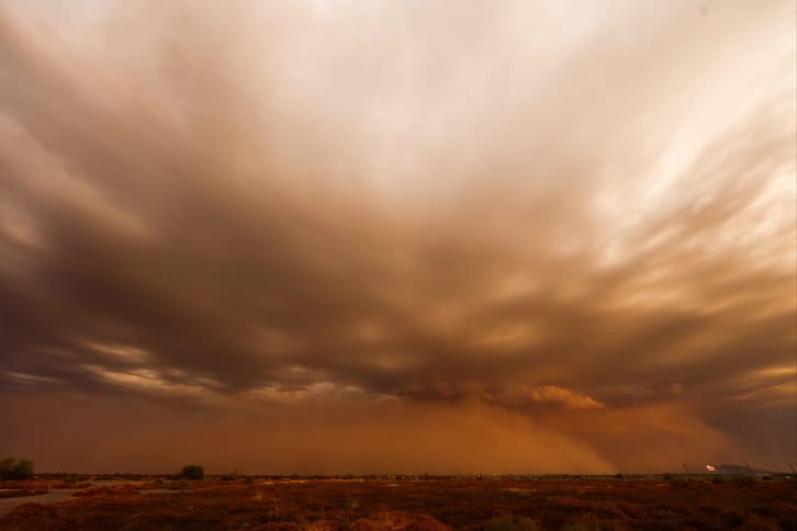 A sandstorm on a day with an orange sky with several clouds and the storm covers the entire environment