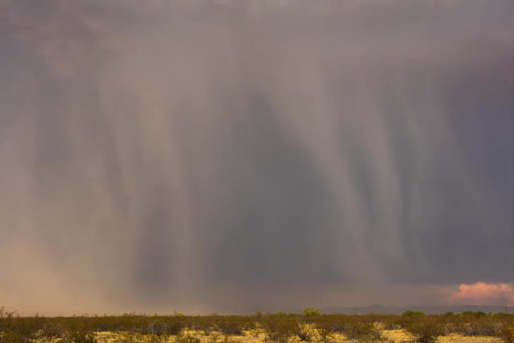 A cloud moving quickly because of the wind and it is lightning striking in the middle of an empty field