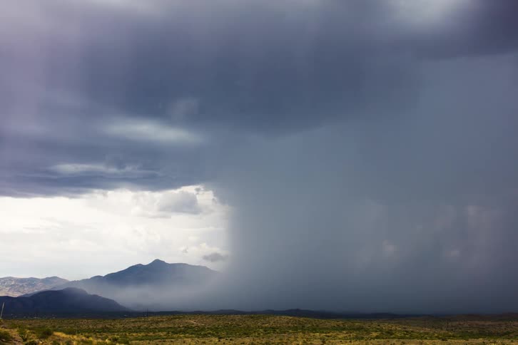 Storm clouds touch the ground in the field in front of mountains