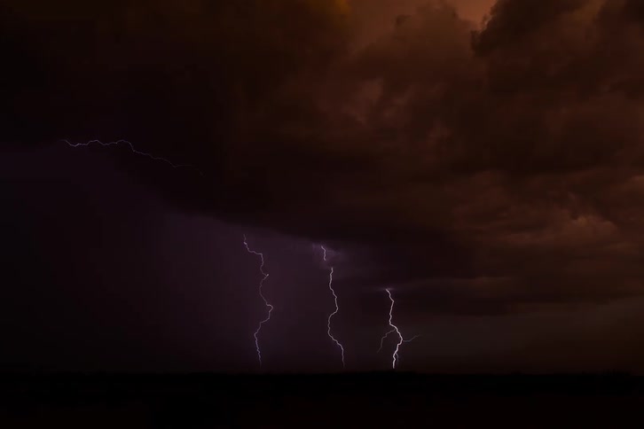 A strong storm of clouds forming in the sky and then a lot of lightning starts to fall and everything starts to get dark
