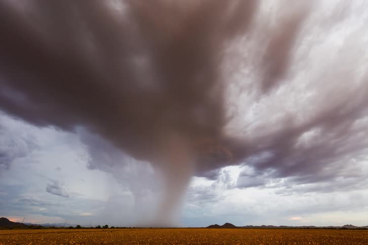 A large tornado in the sky hitting the ground of an empty field and with some lightning falling