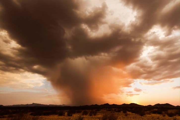 Sun setting over the mountains on the horizon tints storm clouds passing over plains red