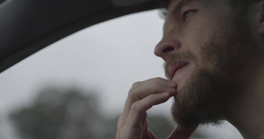 A man rubs his chin while sitting in a car
