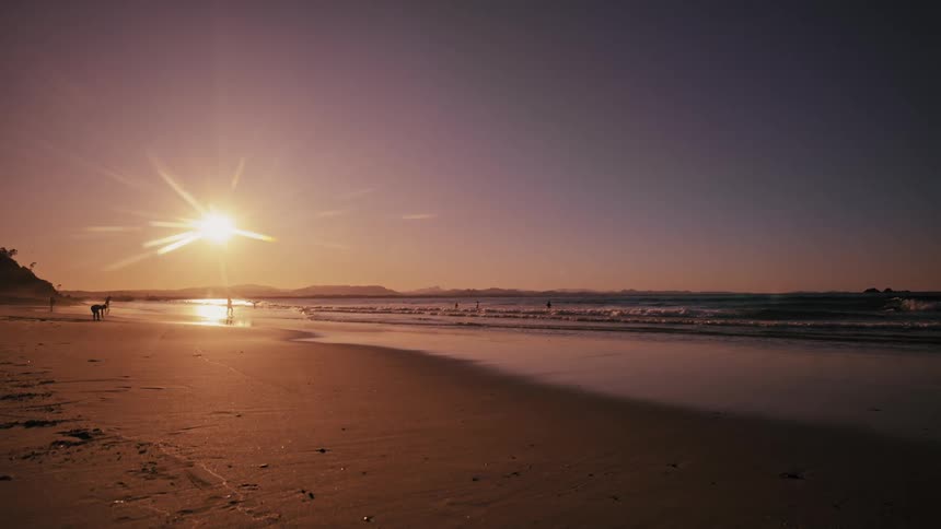 People enjoy the beach while the sun rises in a red tinted sky