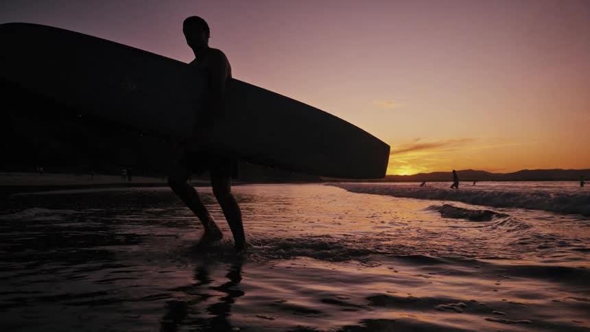 The silhouette of a surfer is carrying his board out of the sea on a morning
