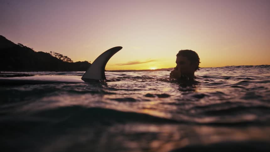 Man in the ocean with his surfboard on a day with purple and orange dawn sky