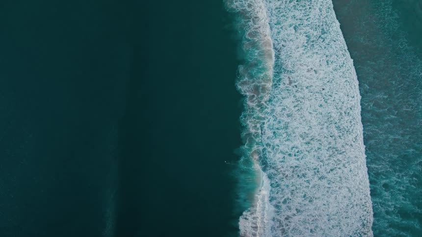 A topdown view of a wave crashing on a dark ocean