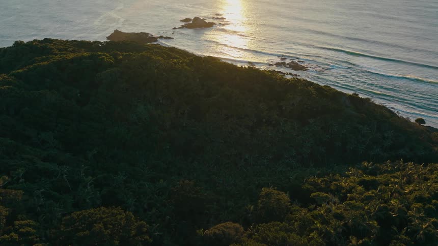 Aerial landscape of a forest island surrounded by the sea and with the sun on the horizon