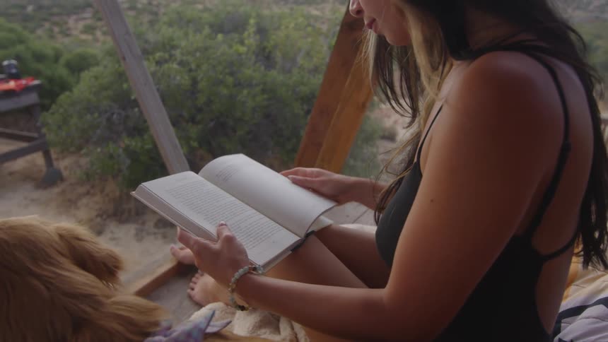 A woman reads a book while sitting on a bed in a glamping tent