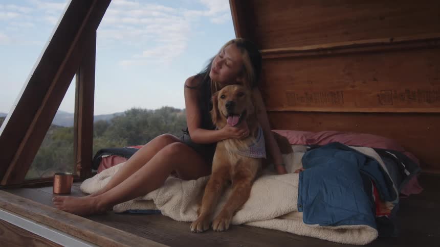 A young woman sits on a deck on the beach being very loving and petting her dog
