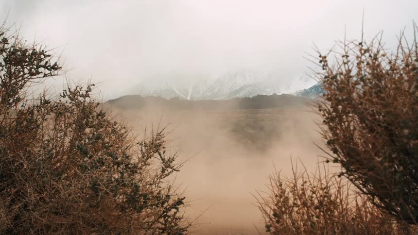 A desert landscape with a cloud of dust rising from the ground