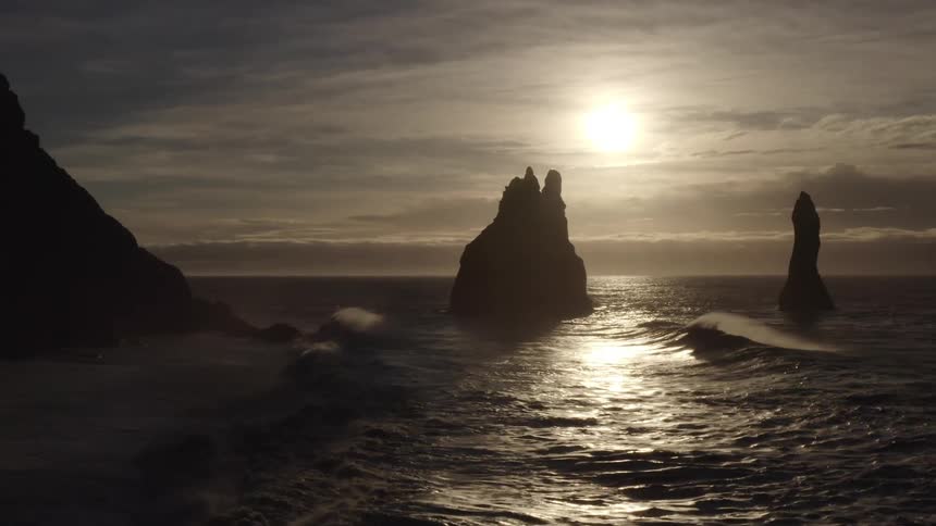 Large rocks with cliffs in the middle of the ocean and the sun on the horizon