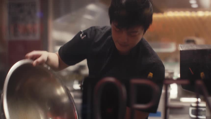 Man inside a restaurant kitchen pouring liquid from a metal basin