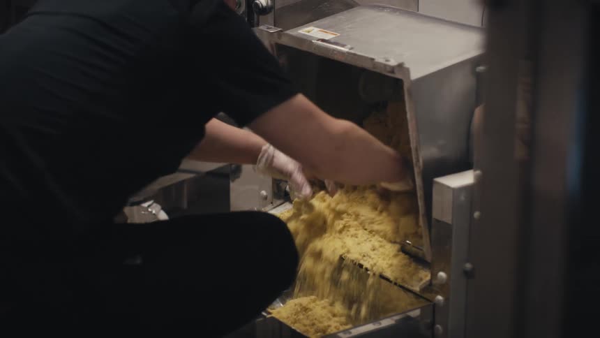 Hands removing pasta from a machine in a restaurant