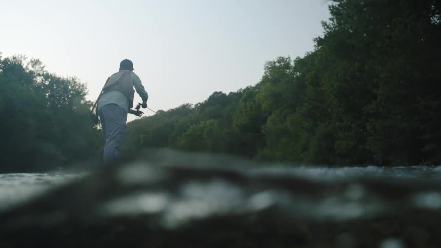 View of moving river water with a man with his back to the camera fishing in the background