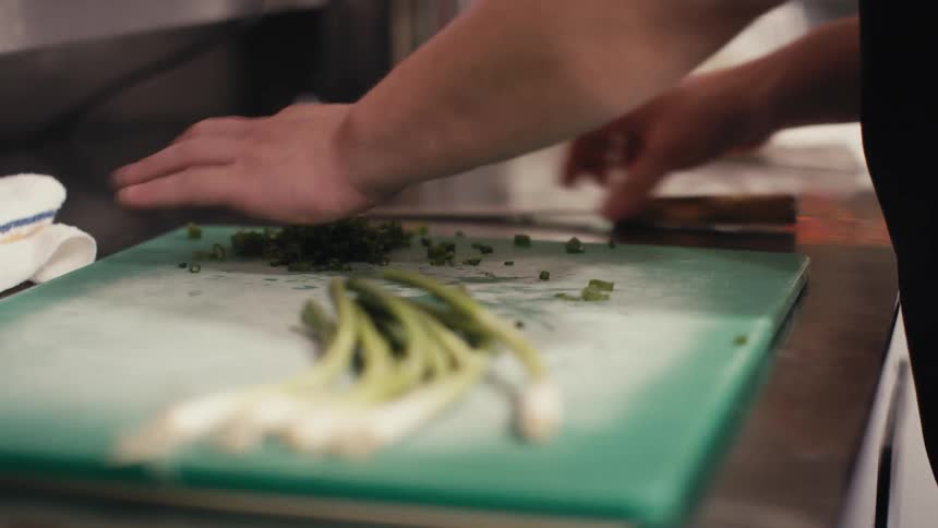 A chef is chopping up scallions in the restaurant kitchen
