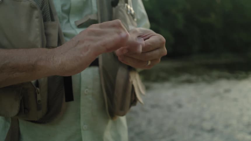 A fisherman carefully ties a fishing line his hands focused on the task