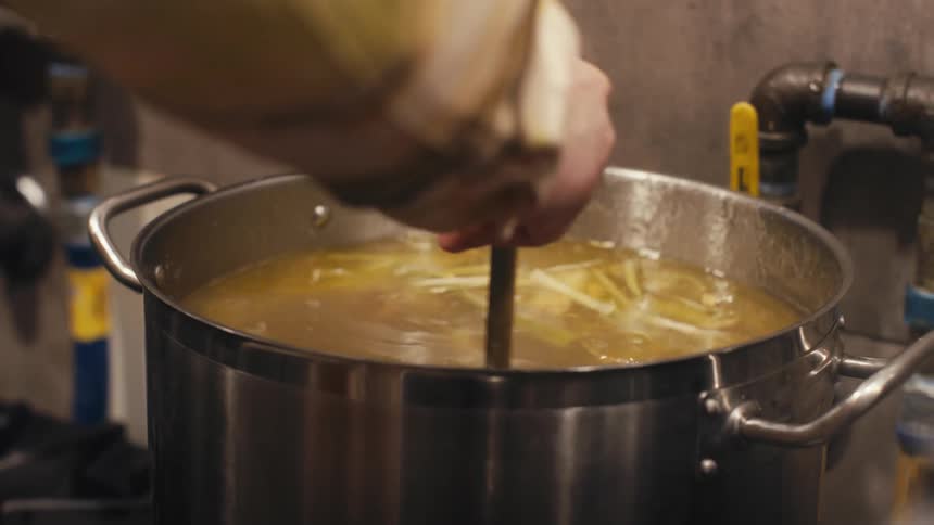 Hand with a metal ladle cooking soup in a pot of boiling water
