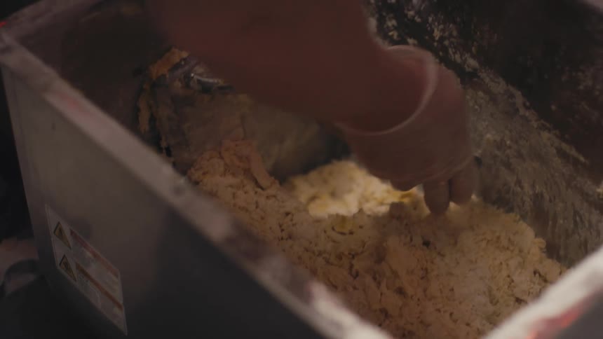 Worker wearing gloves cleans off the paddle in a mixing machine