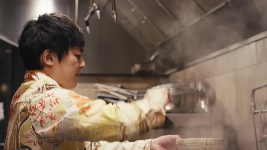 A cook pours hot soup into a bowl