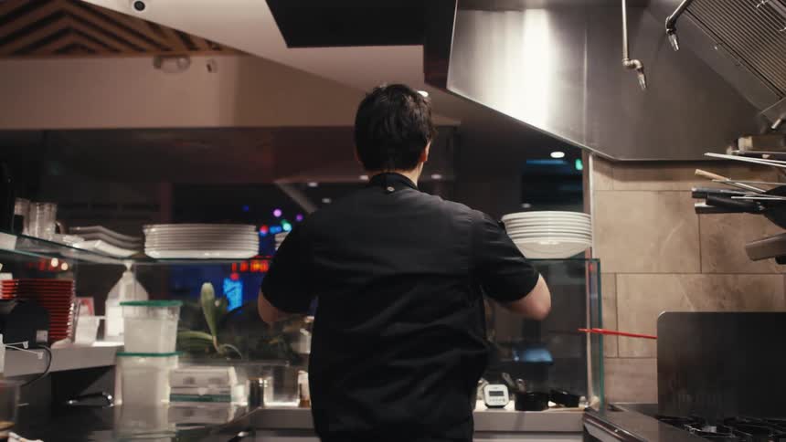 Back view of a man putting on a black jacket while standing in a restaurant kitchen