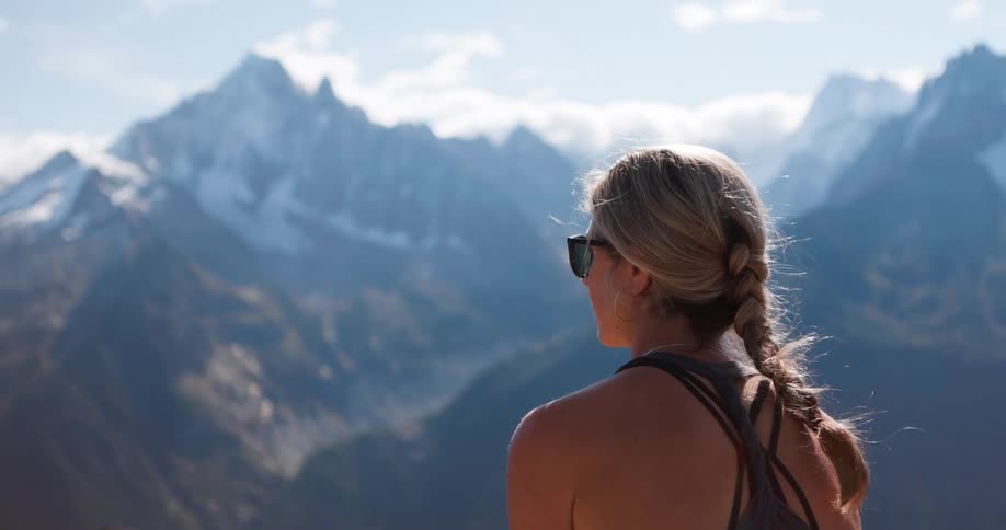 A woman with long blonde hair braided takes in the view of a mountain range