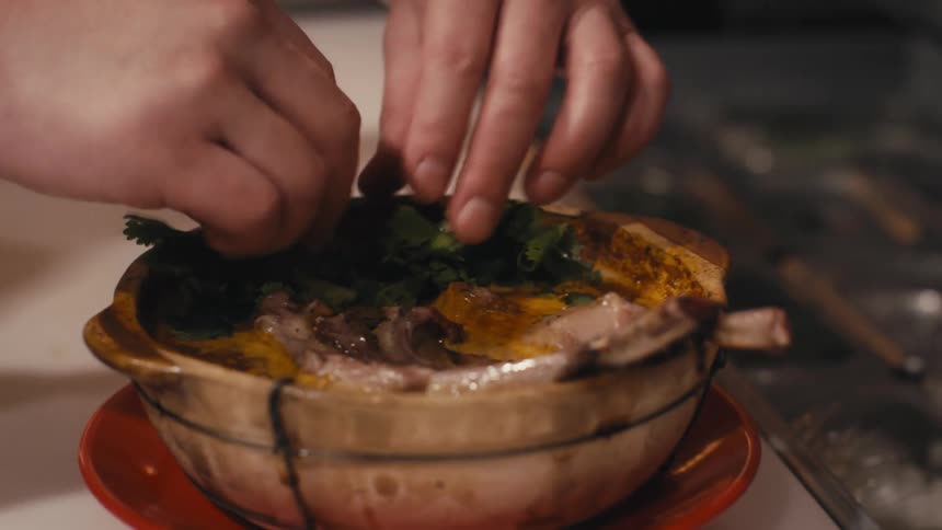 Hands adding greens to a dish in a clay pot