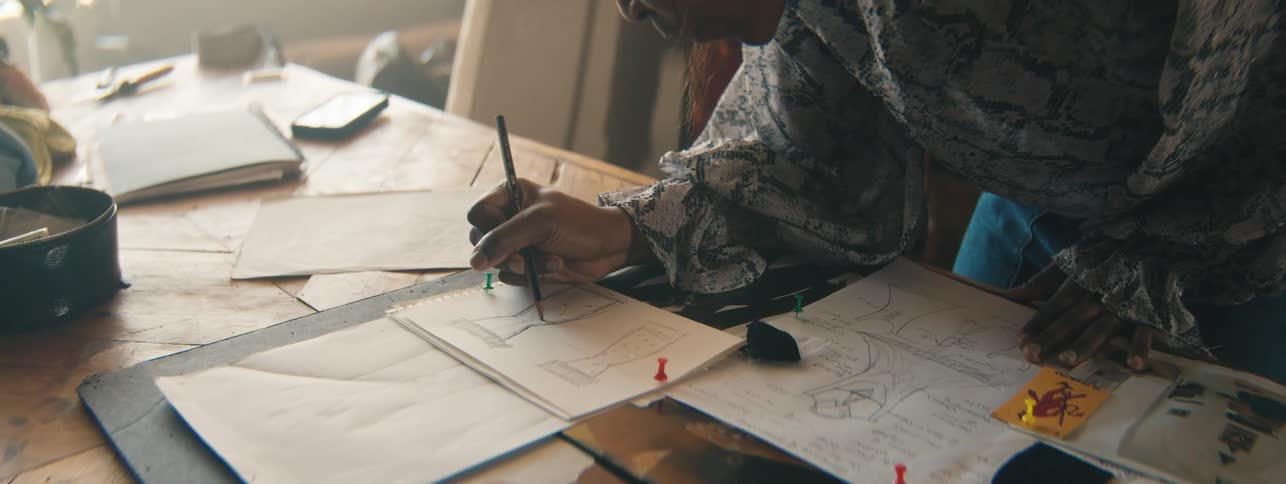 Womans hand with a pencil drawing a dress design on a white sheet of paper on the table