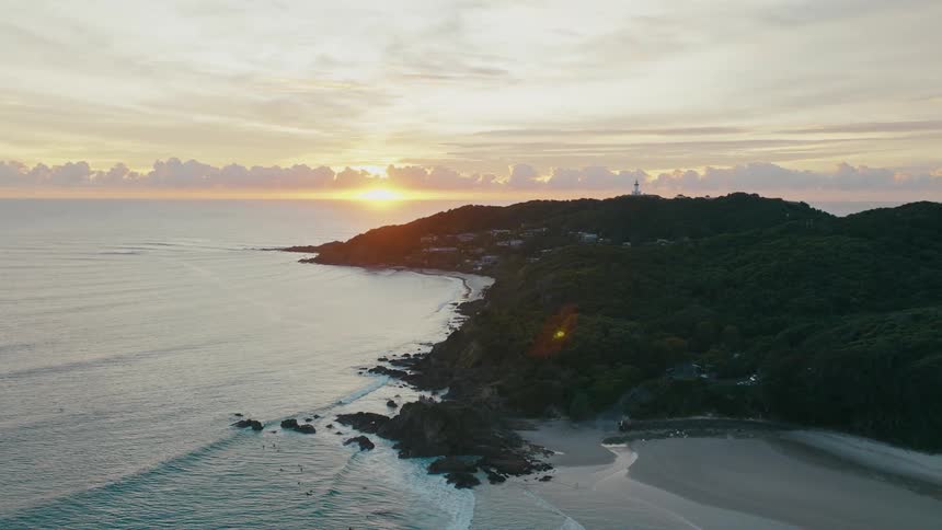 Aerial view of a beach and island with golden sun on the horizon