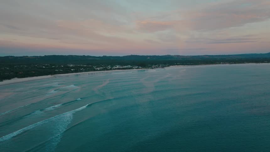 An aerial view of a sea with some waves heading towards a coast that is full of vegetation