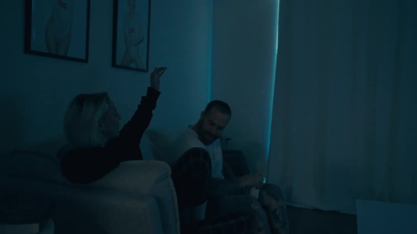 A young couple sitting on a couch on a dimly lit room at home