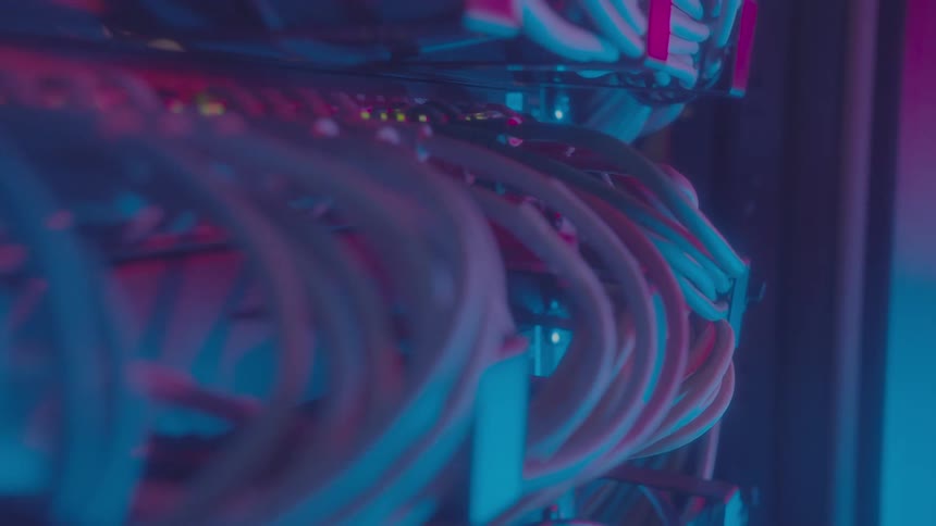 Closeup of a server rack with numerous cables under pink and red lights