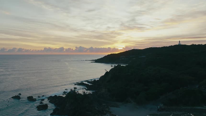 A serene beach at sunset with a lighthouse perched on a distant cliff