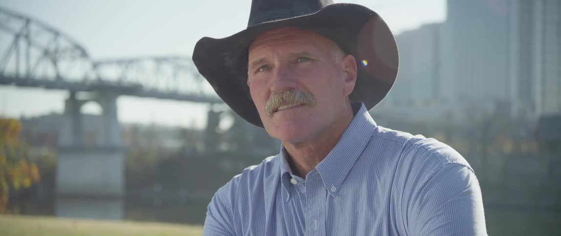 A man in a cowboy hat sits in a city park