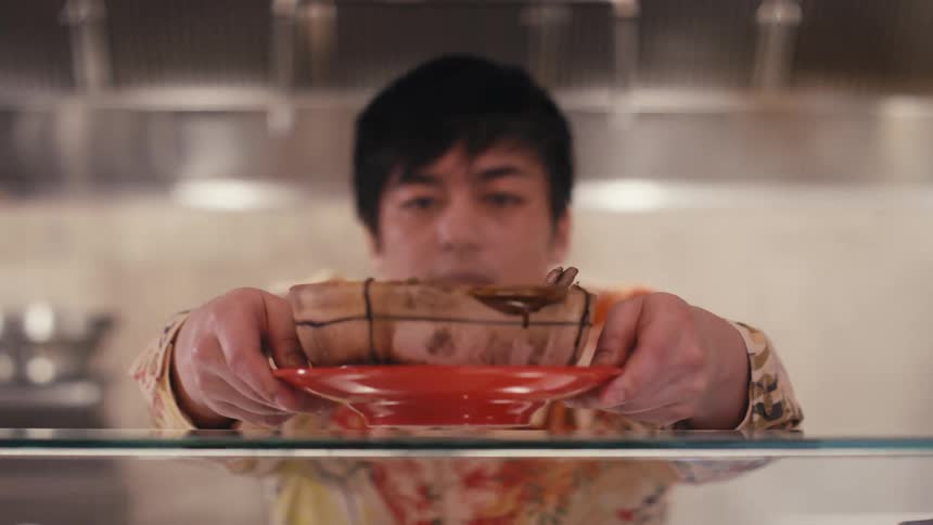 Chef in a restaurant kitchen placing a ceramic bowl on top of a glass shelf