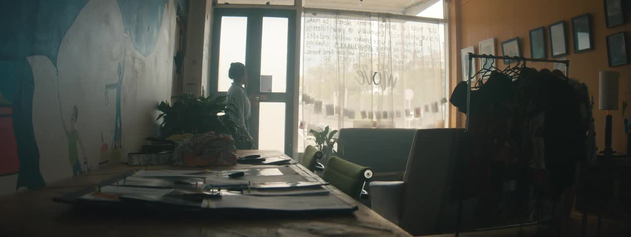 A woman holding a bag is walking through a glass door and then she places the bag on a table