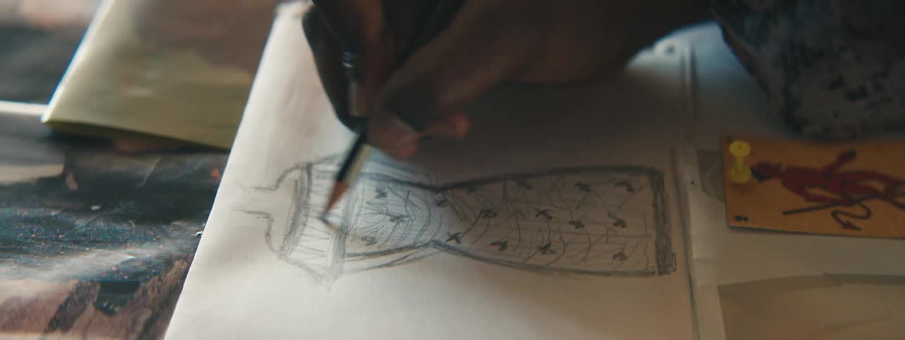 A human hand using a pencil to draw a picture of a dress on white paper