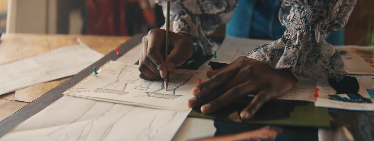Hands of a woman drawing dresses on a paper on the table