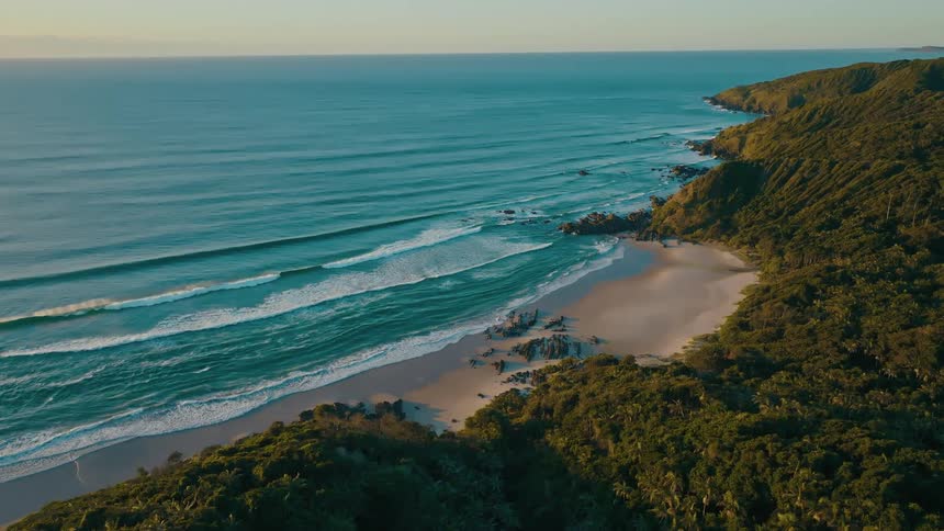 A pristine coastline with rolling waves crashing on a sandy beach surrounded by lush green forest