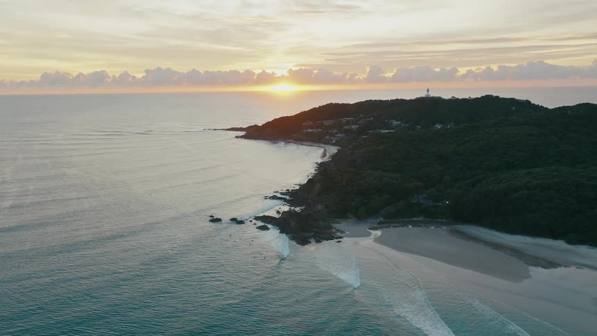 Aerial view of an island surrounded by a beach and the sun rising on the horizon
