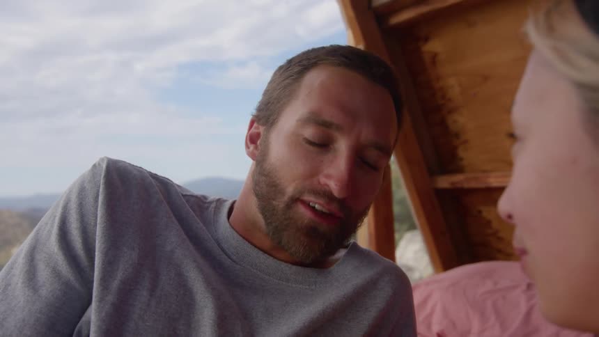 Man and woman in a cabin talking and mountains in the background