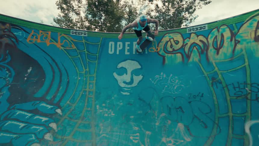 Tattooed man in tank top doing skateboard tricks on a circular track