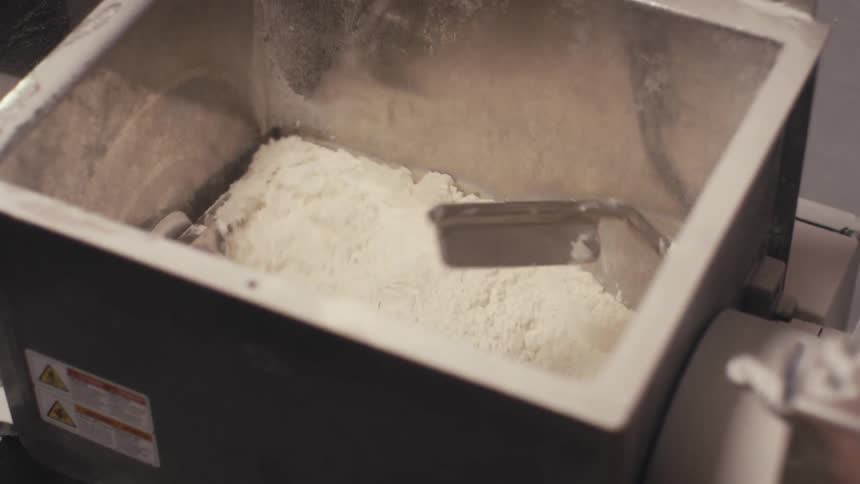 A container filled with flour being sifted by rotating metal blades