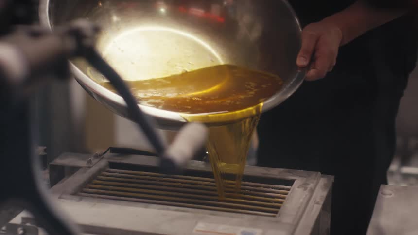 Person holding a bowl of oil and pouring it into a kitchen appliance in a restaurant