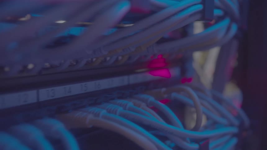 Closeup of a server rack with numerous cables under pink and red lights