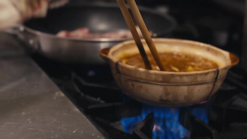 Hand with chopsticks preparing ramen in a bowl on the stove