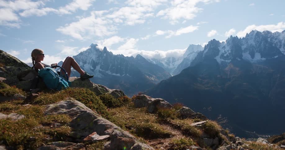 Woman sitting between rocks on a cliff with a panoramic view of snowy mountains