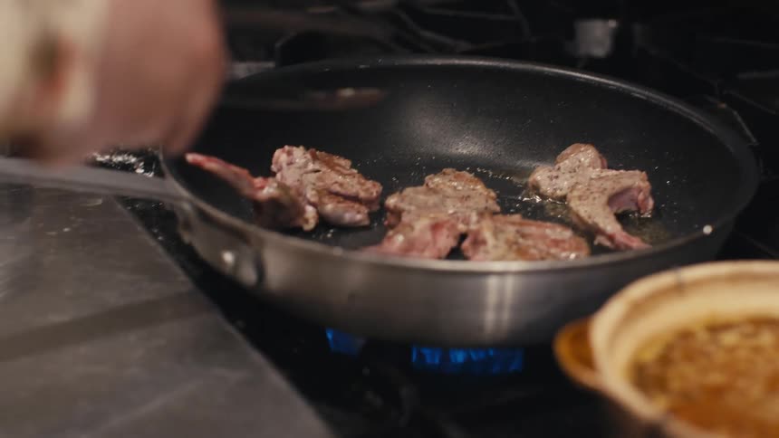 A chef's hand flipping meat in a frying pan