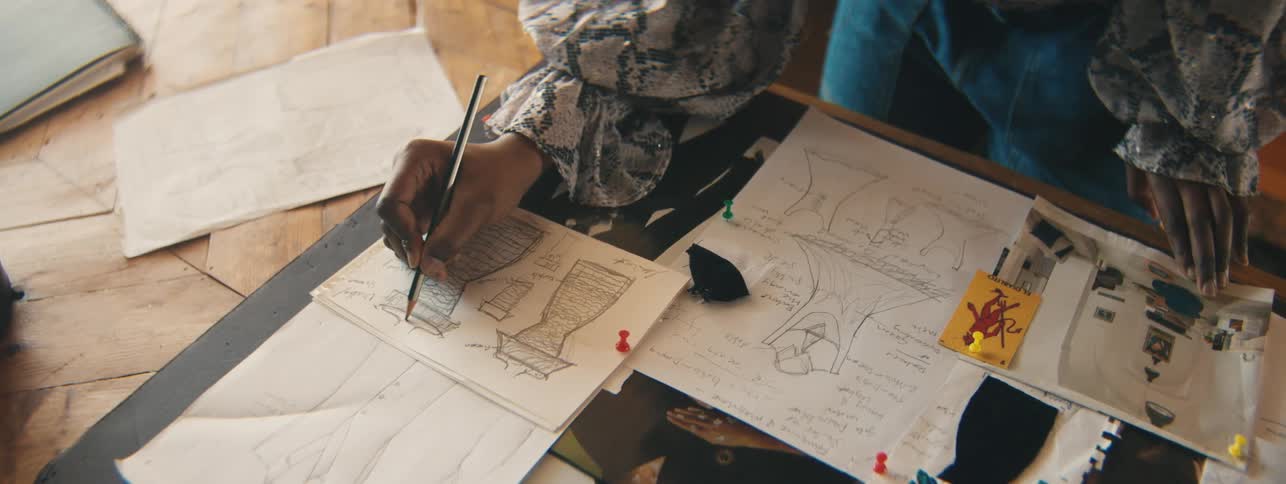 Top view of a female hand holding a pencil and drawing the silhouette of a dress