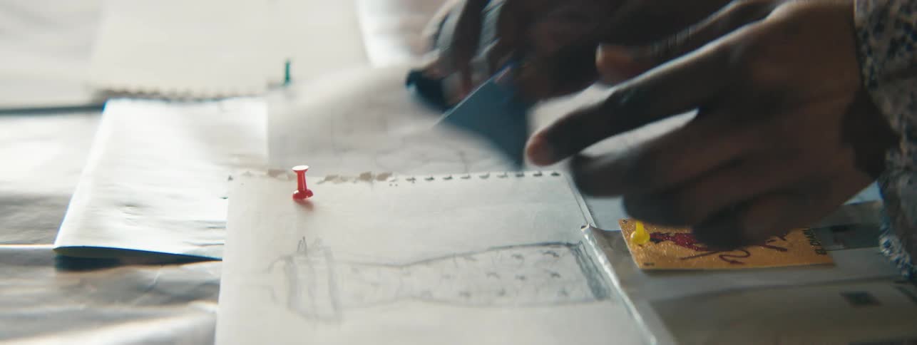 Persons hand placing small pieces of fabric on top of fashionable dress designs